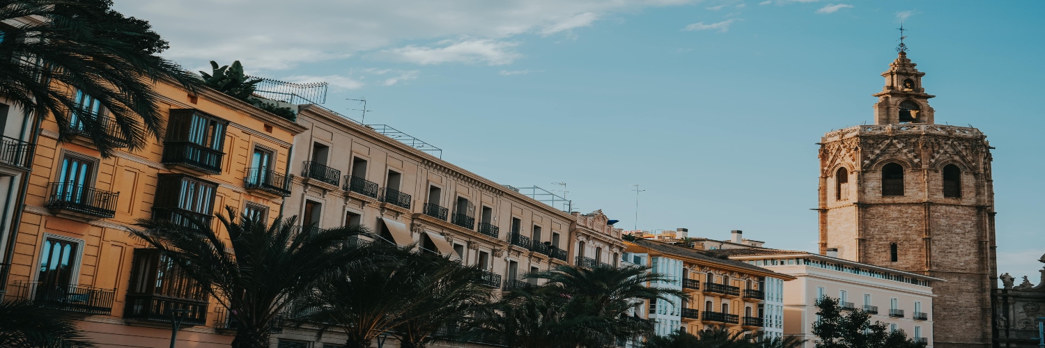 A tall tower of Valencia Cathedral rises above palm trees in the foreground, showcasing a blend of architecture and nature.