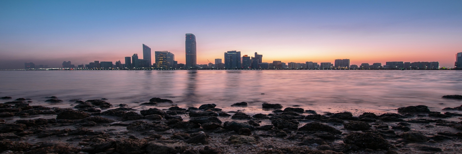 Abu Dhabi skyline at sunset, showcasing modern architecture against a vibrant orange and purple sky.