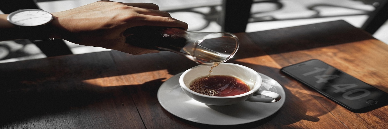 A person pours coffee from a pot into a cup on a table at Coffee Cafe in Canberra.