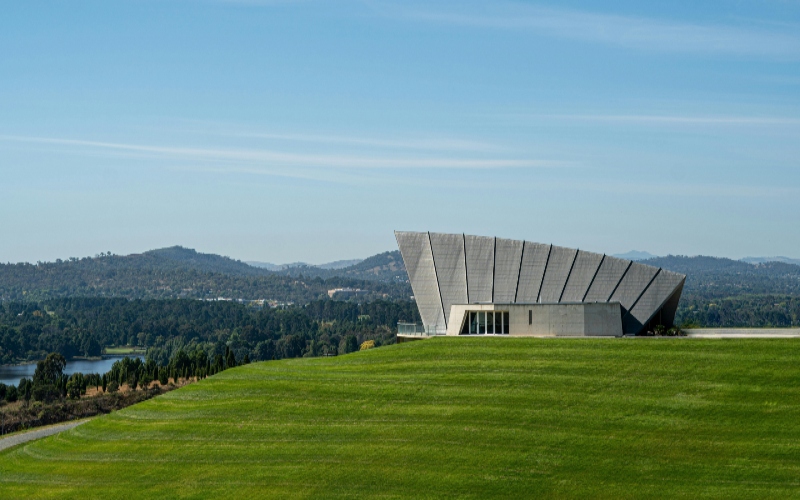 A modern building atop a hill during the open day at the National Arboretum in Canberra, surrounded by lush greenery.