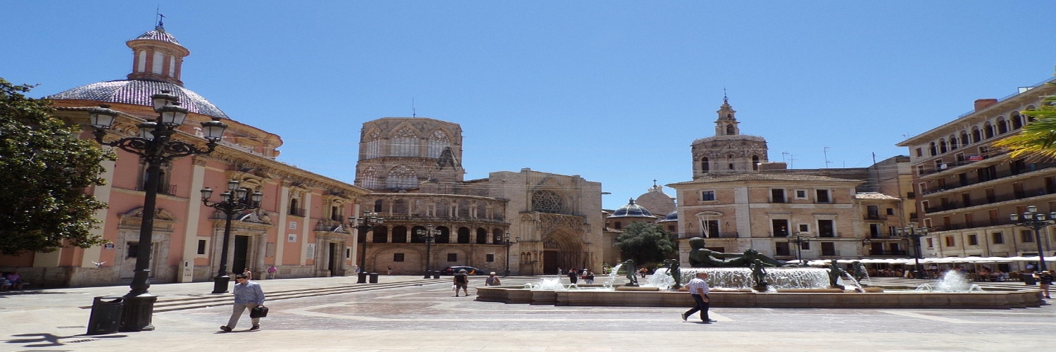 A city square featuring a fountain, a clock tower, and the Valencia Cathedral in the background.
