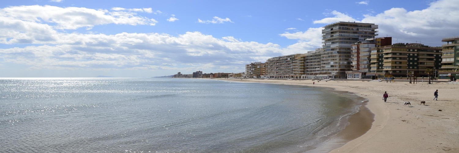 A beach near Valencia with people walking along the shore and buildings visible in the background.