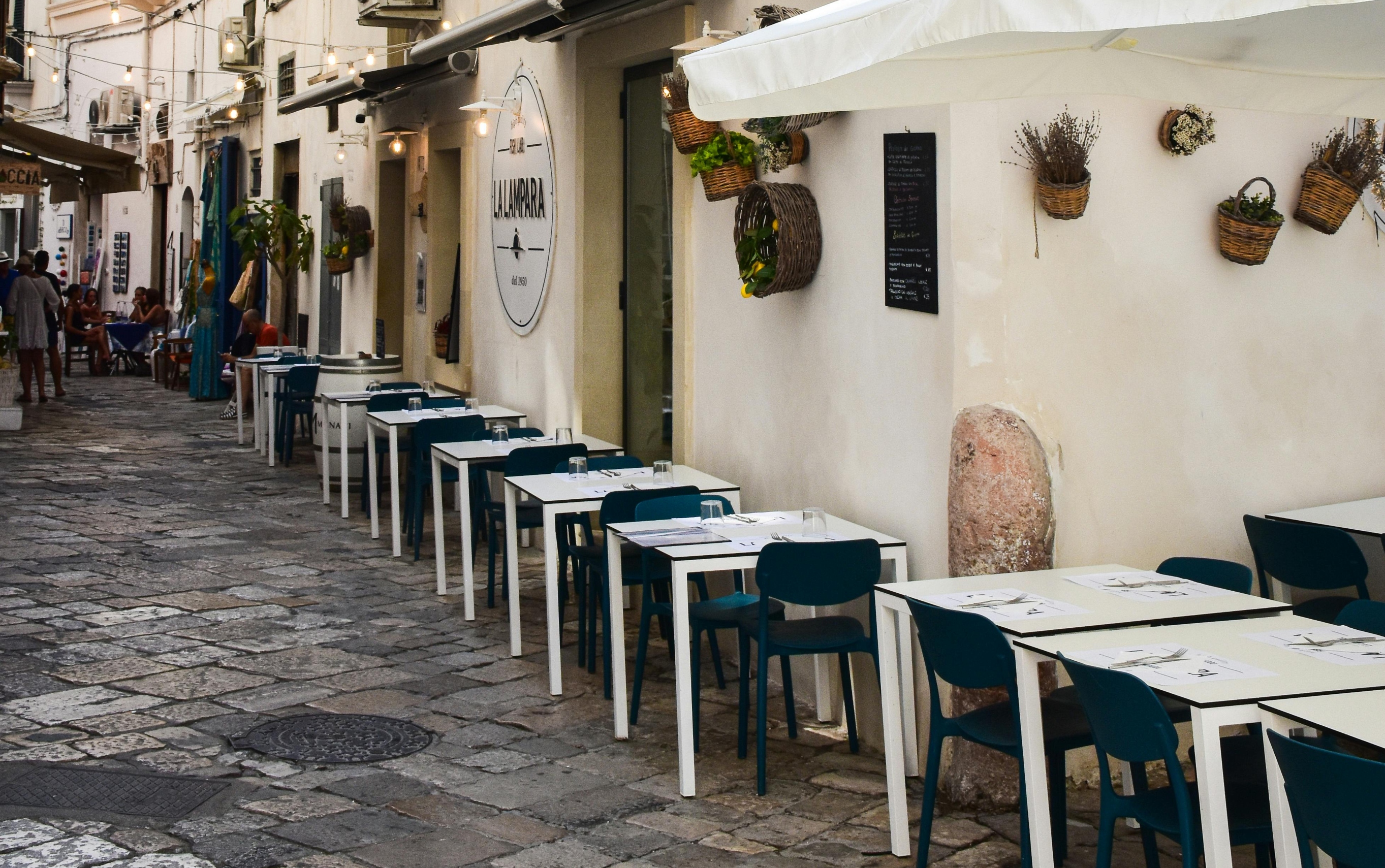 Outdoor seating with tables and chairs lining a narrow street in a cafe in Bari, Italy.
