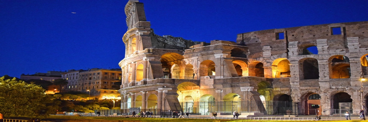 The Colosseum in Rome illuminated at night, showcasing its ancient architecture against a dark sky.