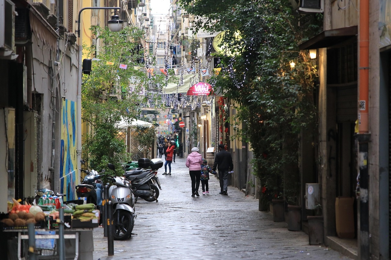 A narrow street in Naples' Historic Quarter, bustling with people walking and enjoying the vibrant atmosphere.