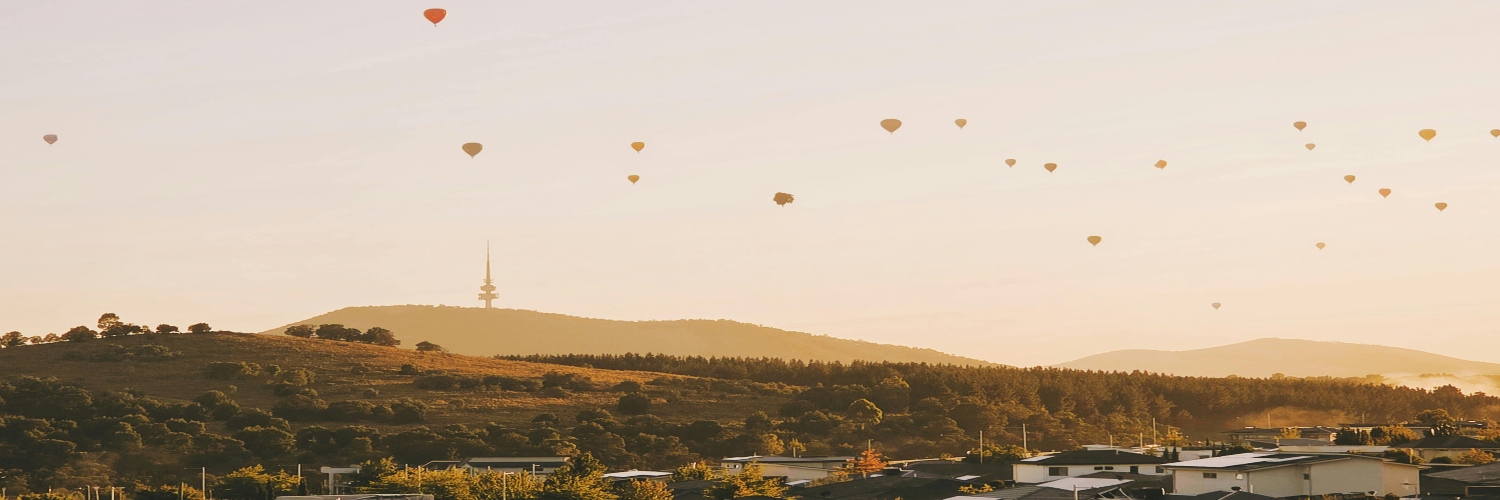 A colorful array of hot air balloons floats over Canberra on a sunny summer day, creating a vibrant cityscape.