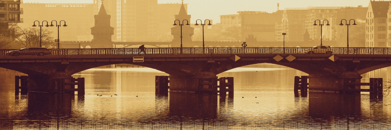 A winter scene of a bridge over a river, with snow-covered buildings of Berlin visible in the background.