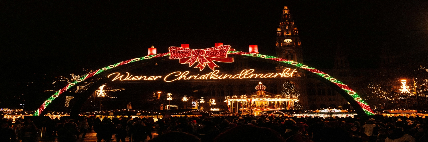 Entrance to the Christmas Market in Vienna, adorned with lights and bustling with people enjoying the festive atmosphere.