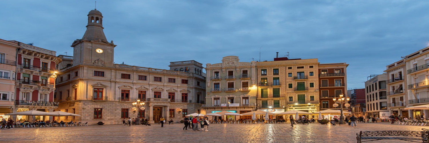 A bustling city square in Reus featuring a prominent clock tower surrounded by shops and visitors enjoying the atmosphere.