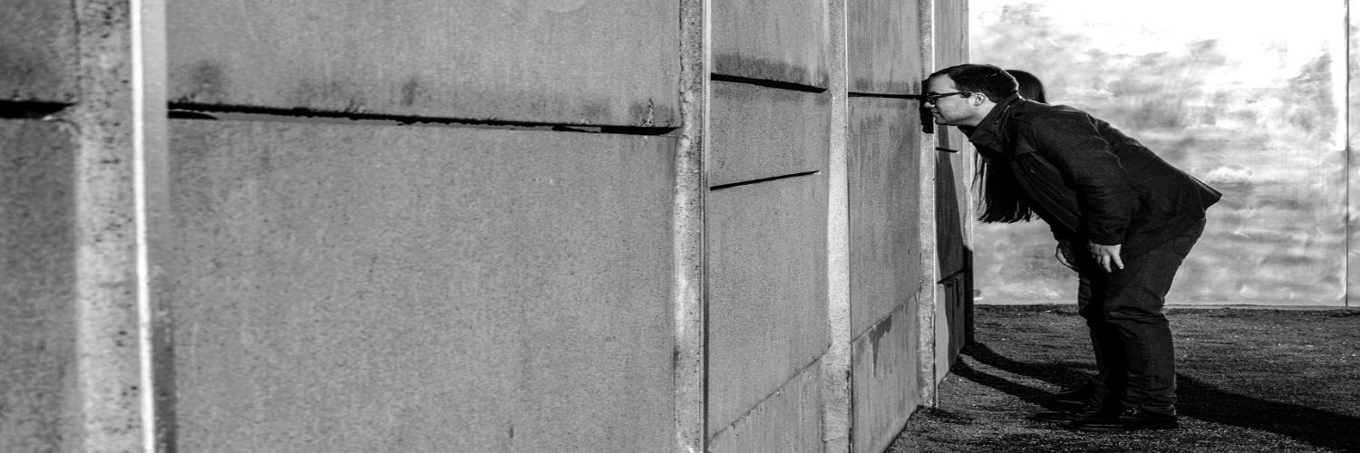 At the Berlin Wall Memorial, a man leans against the wall, his head in his hands, expressing deep contemplation.