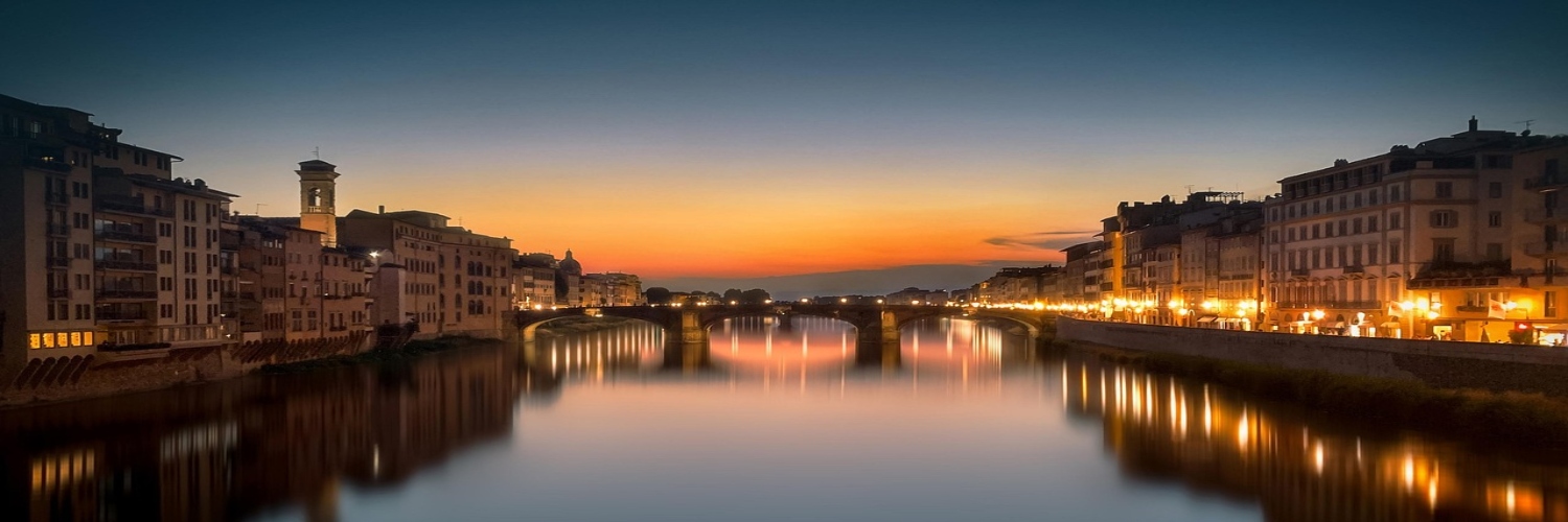 The river in Florence glows with warm hues during a summer sunset, reflecting the vibrant colors of the sky.