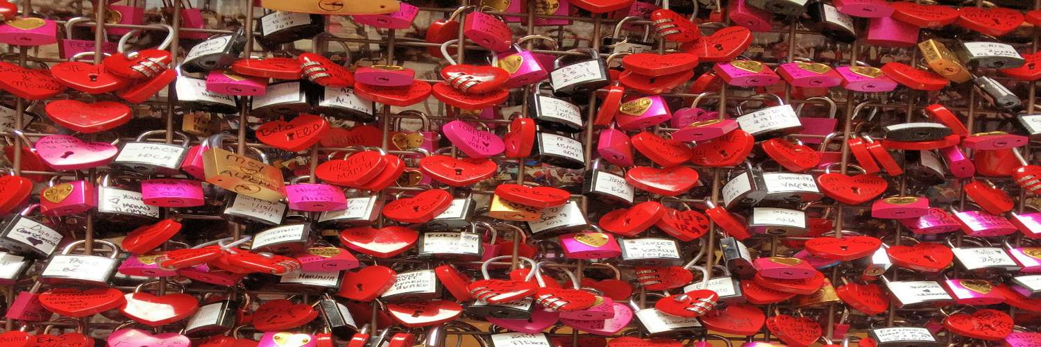 A collection of red heart-shaped locks hanging on a grey metal wall, symbolizing love and commitment in Verona.