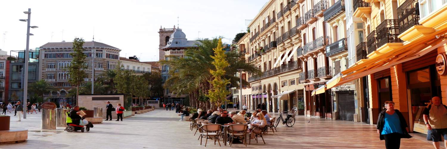 A bustling Valencia street filled with people walking and dining at outdoor tables, showcasing the city's vibrant atmosphere.