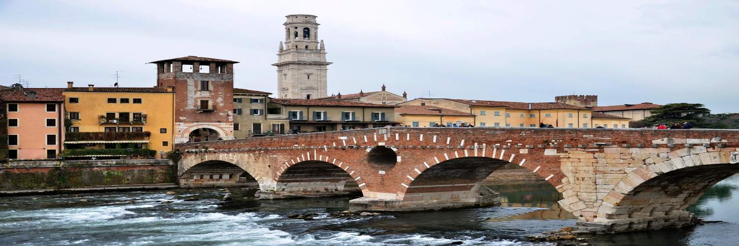 Stone bridge over a river in Verona, with a clock tower visible in the background against a clear sky.