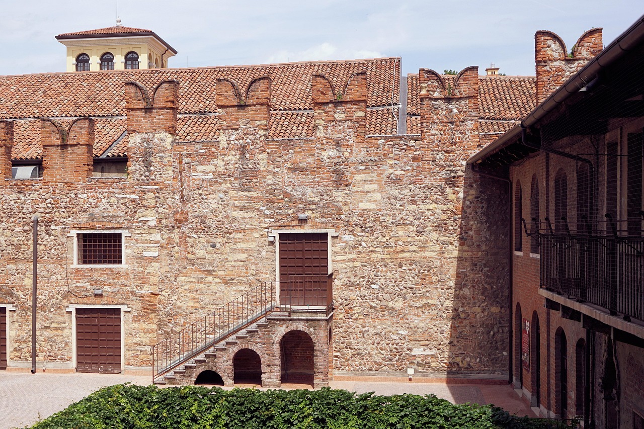 The courtyard of Casa Di Giulietta in Verona, showcasing a brick building and an ornate gate.