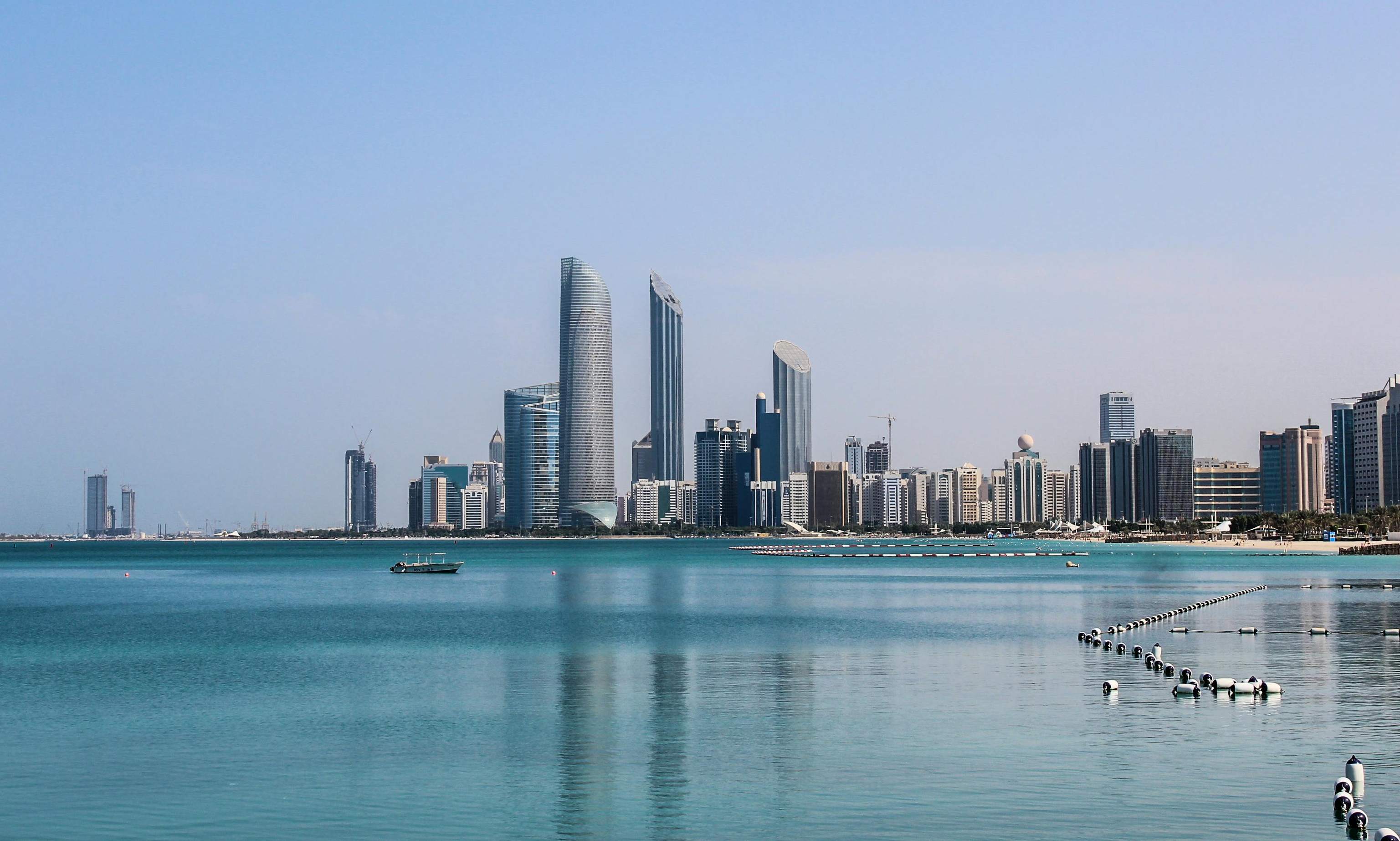 A clear day view of Abu Dhabi's skyline from the water, showcasing modern architecture and vibrant city life.