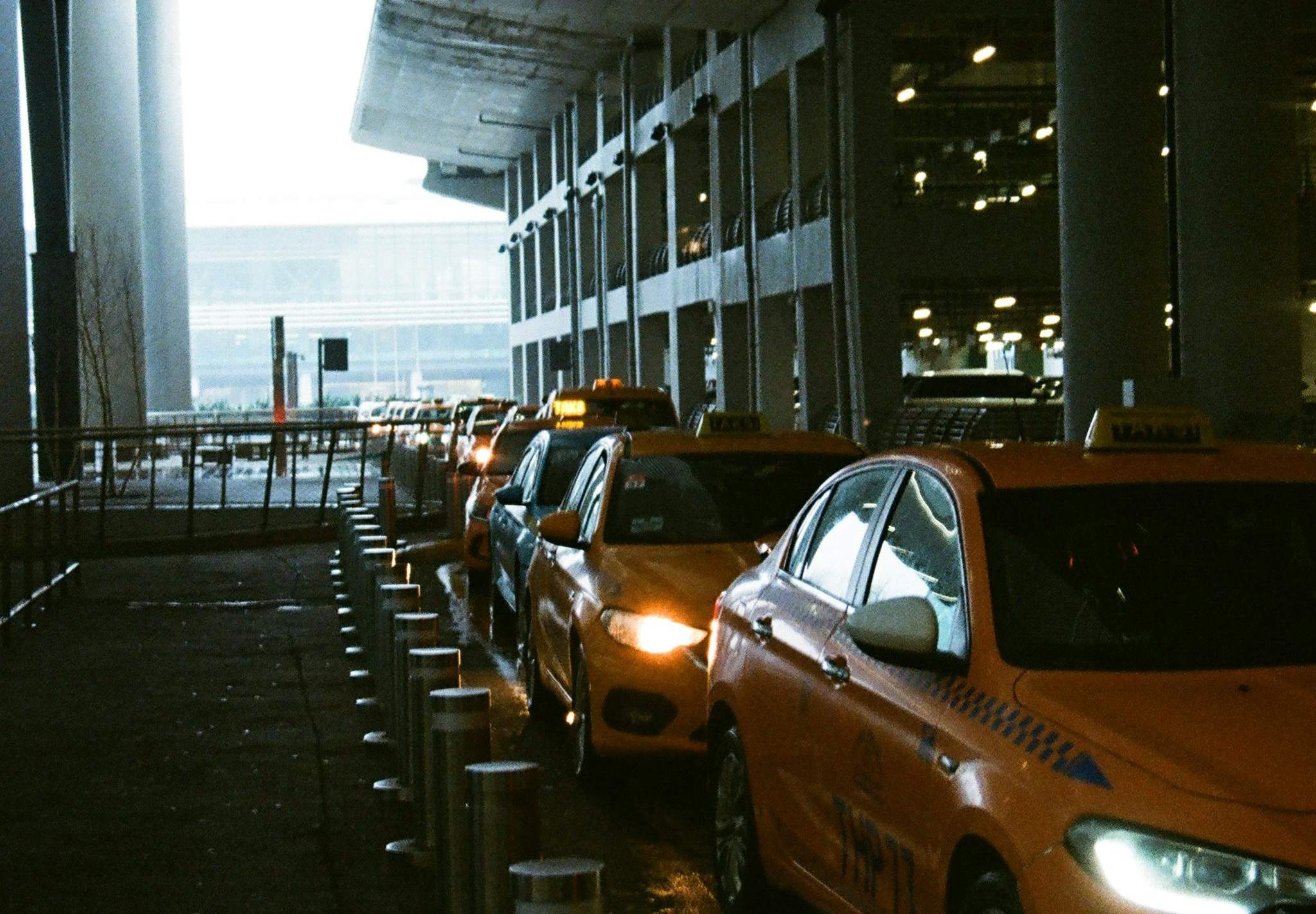 A large building featuring a clock tower, with an airport taxi in front, set in London.
