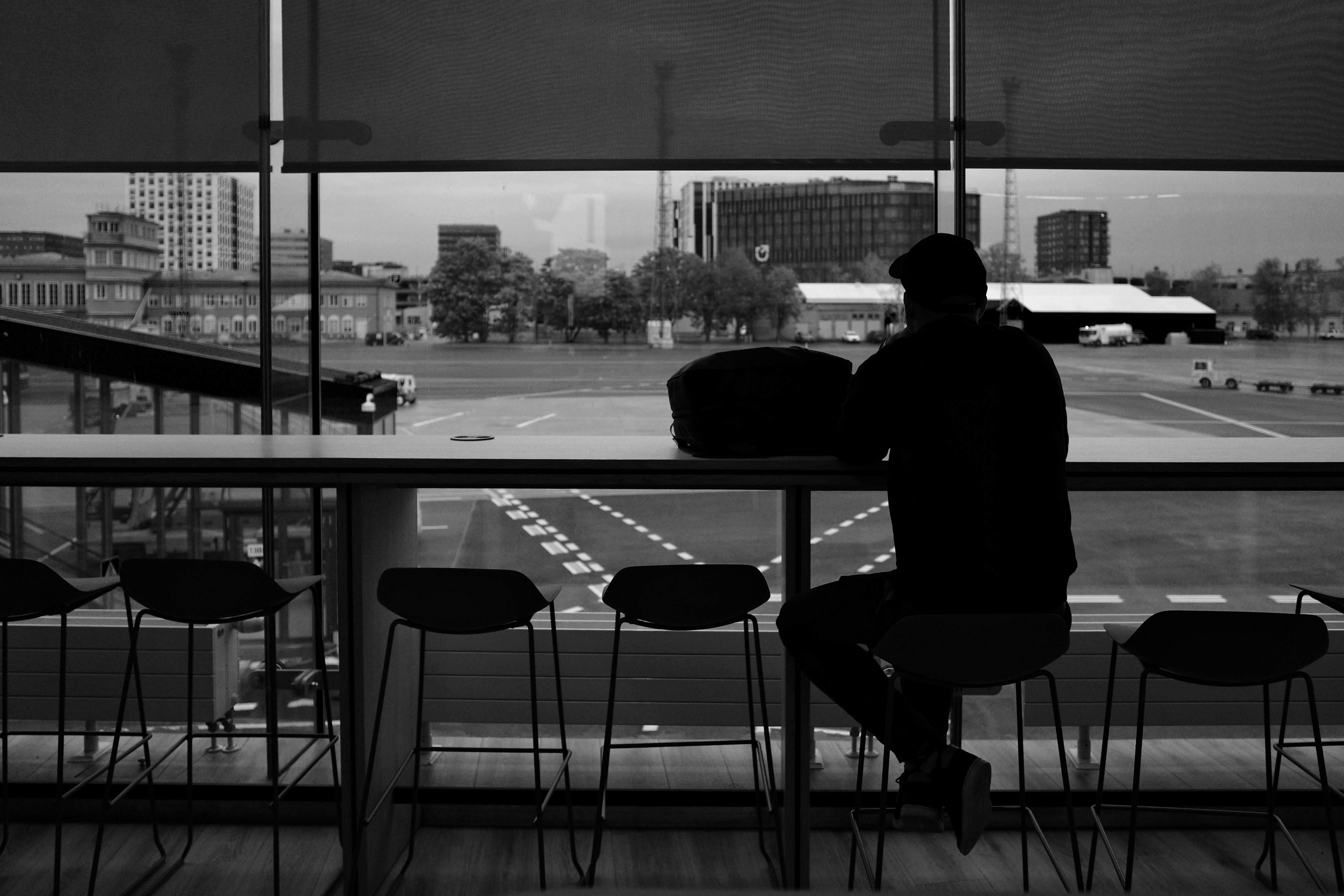 A silhouette of a man sitting at a table, gazing out a window at Dubai Airport, waiting for his flight.