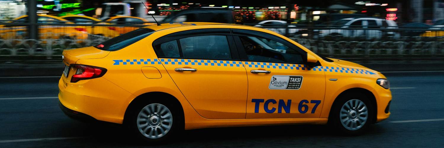 A taxi cab driving down a street at night, serving as a pre-booked airport transfer.