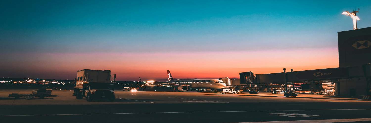 An airplane parked at an airport during sunset, with vibrant orange and purple skies in the background.