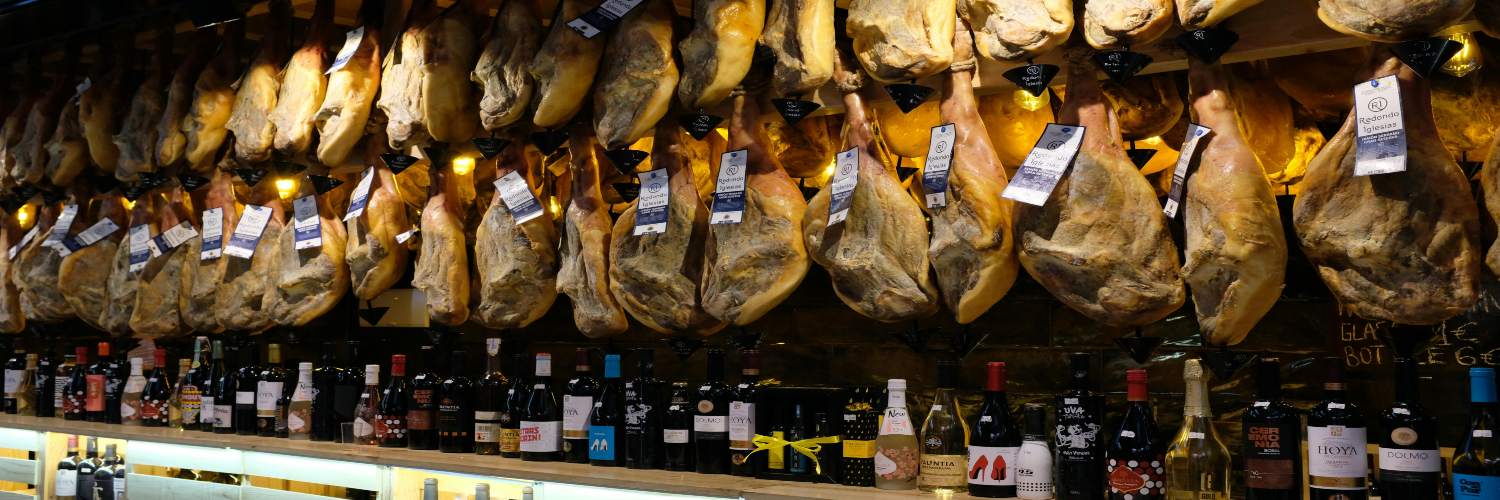 A bar filled with wine bottles and meat hanging on the wall, adorned with fish decorations, located in Barcelona.