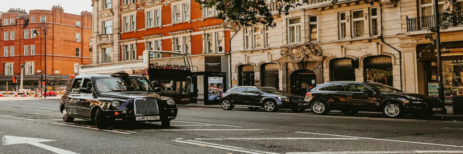 A black taxi driving along a city street, representing airport transfer options in London.