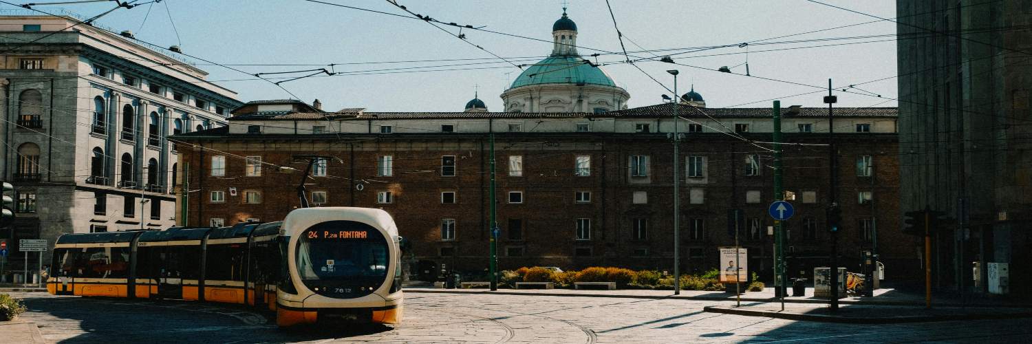 A tram travels down a street in Milan, passing in front of a historic building.
