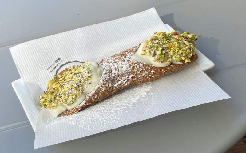 A delicious Italian cannoli topped with cream and pistachios, resting on a white napkin.
