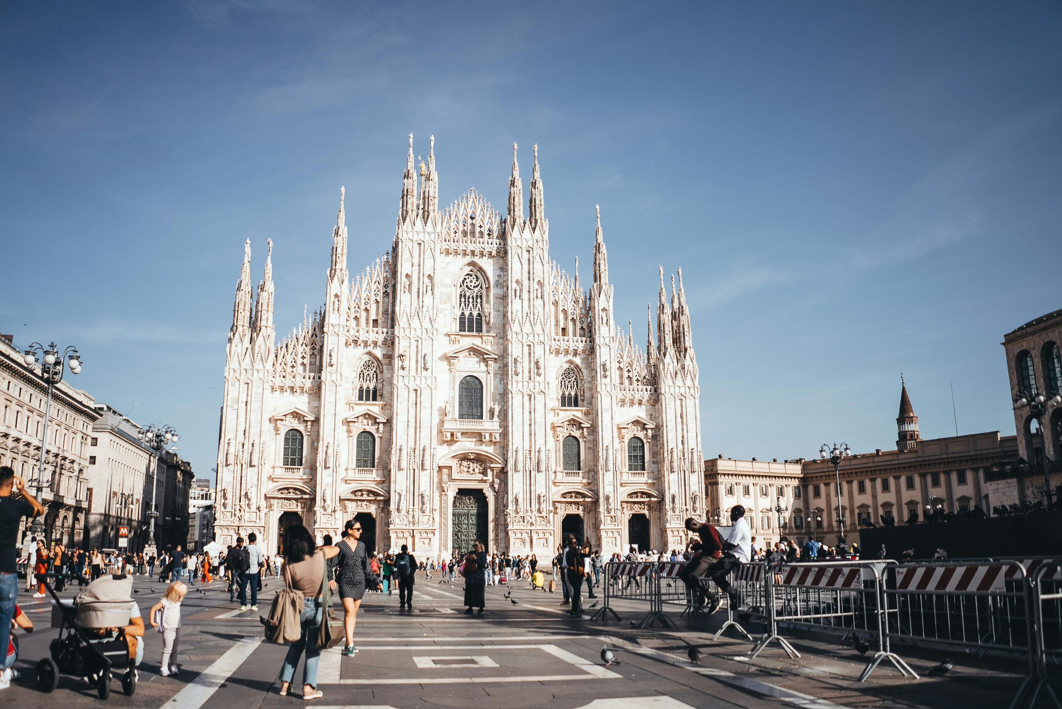 The Duomo in Milan, Italy, showcasing its intricate Gothic architecture and towering spires against a clear blue sky.
