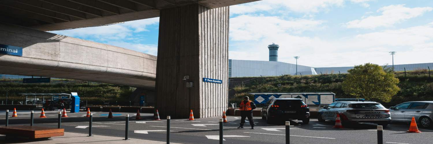Cars parked under a bridge near a large building at Paris Charles de Gaulle Airport.