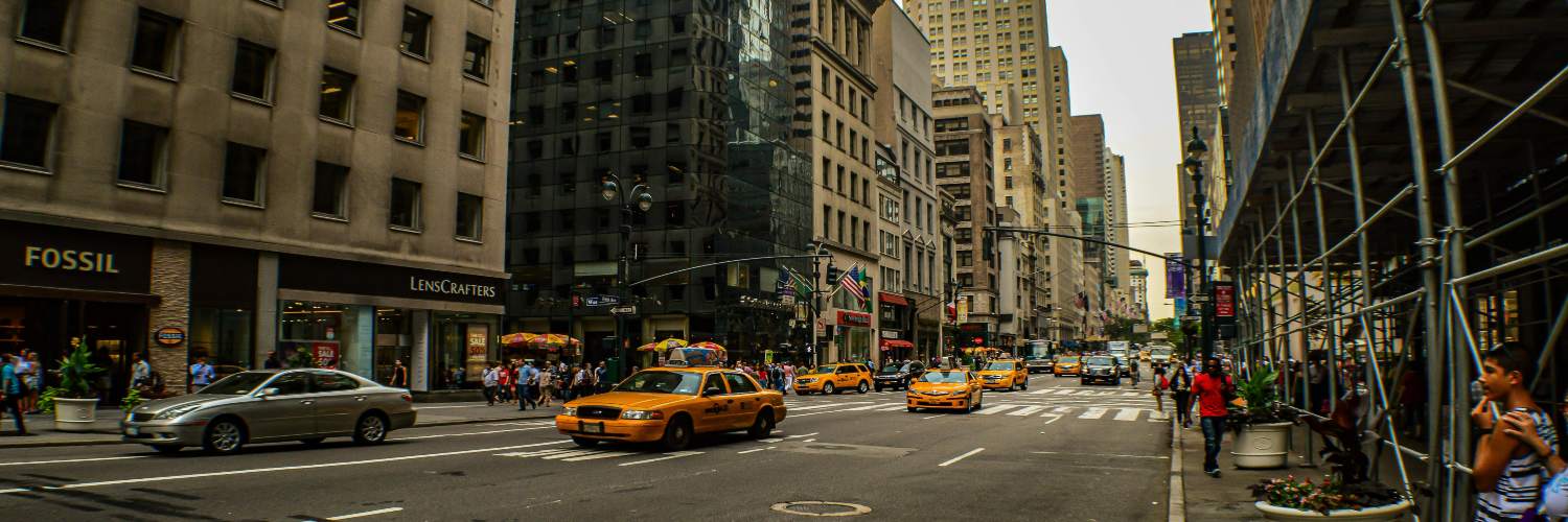 Yellow taxi cab driving through New York City streets at night, illuminated by city lights.
