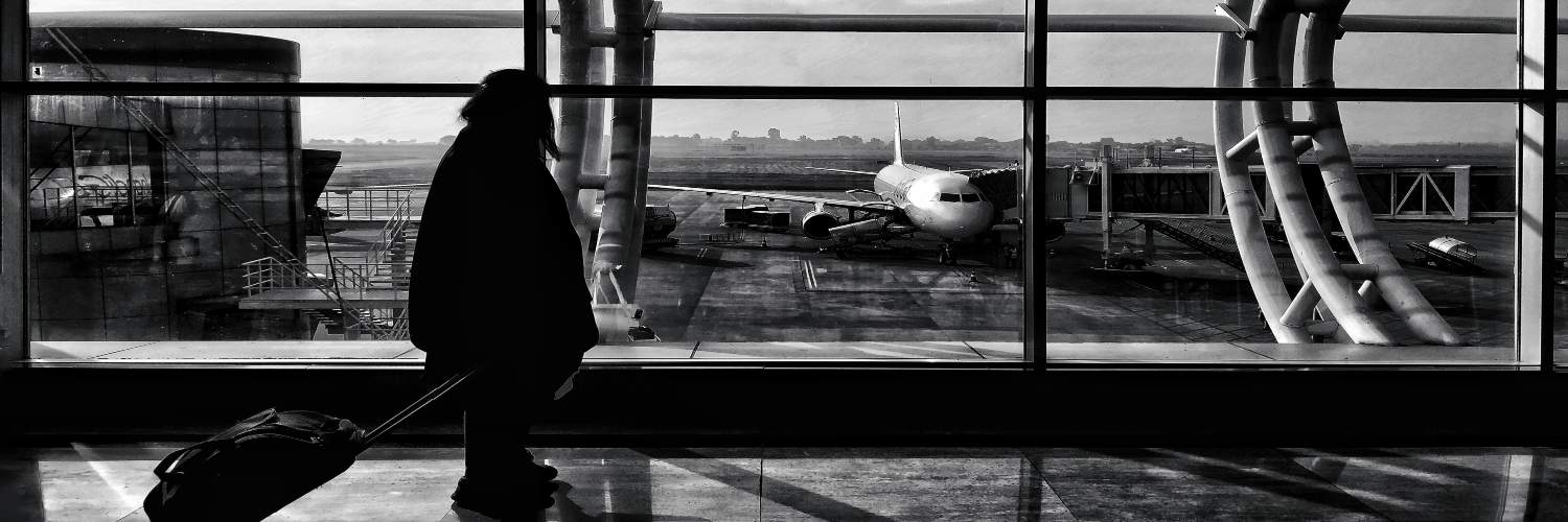 A female traveler stands with a suitcase in front of a large window, looking out at the view beyond.