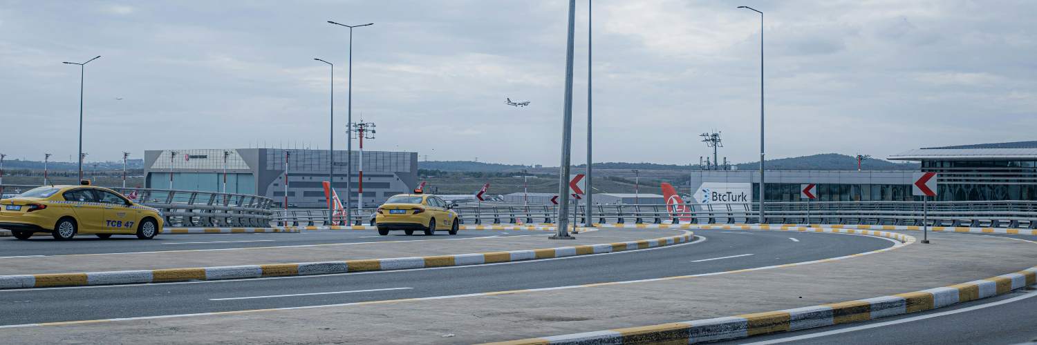 A yellow airport taxi drives on a highway alongside a modern building.
