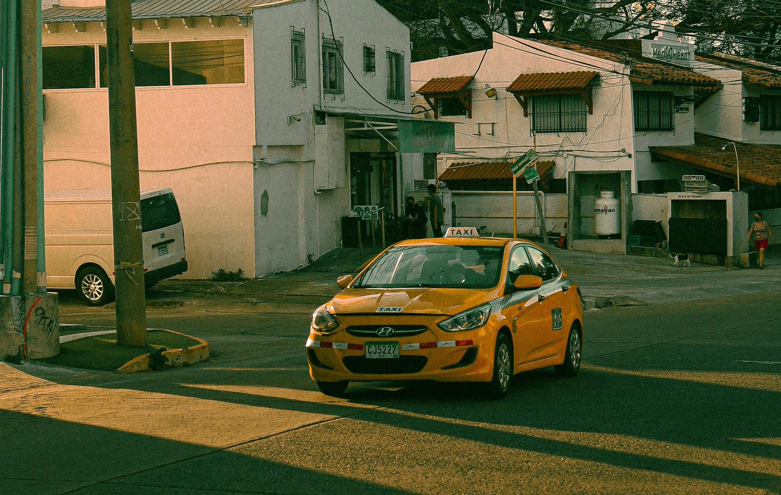 Yellow taxi driving through a residential street, representing Alicante taxi transfer and airport transportation services.
