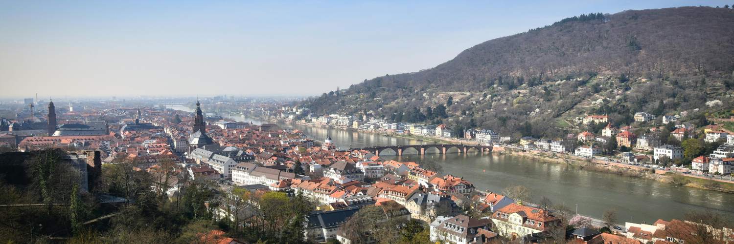 View of Heidelberg, Germany, featuring the iconic bridge crossing the Neckar River with historic buildings in the background.