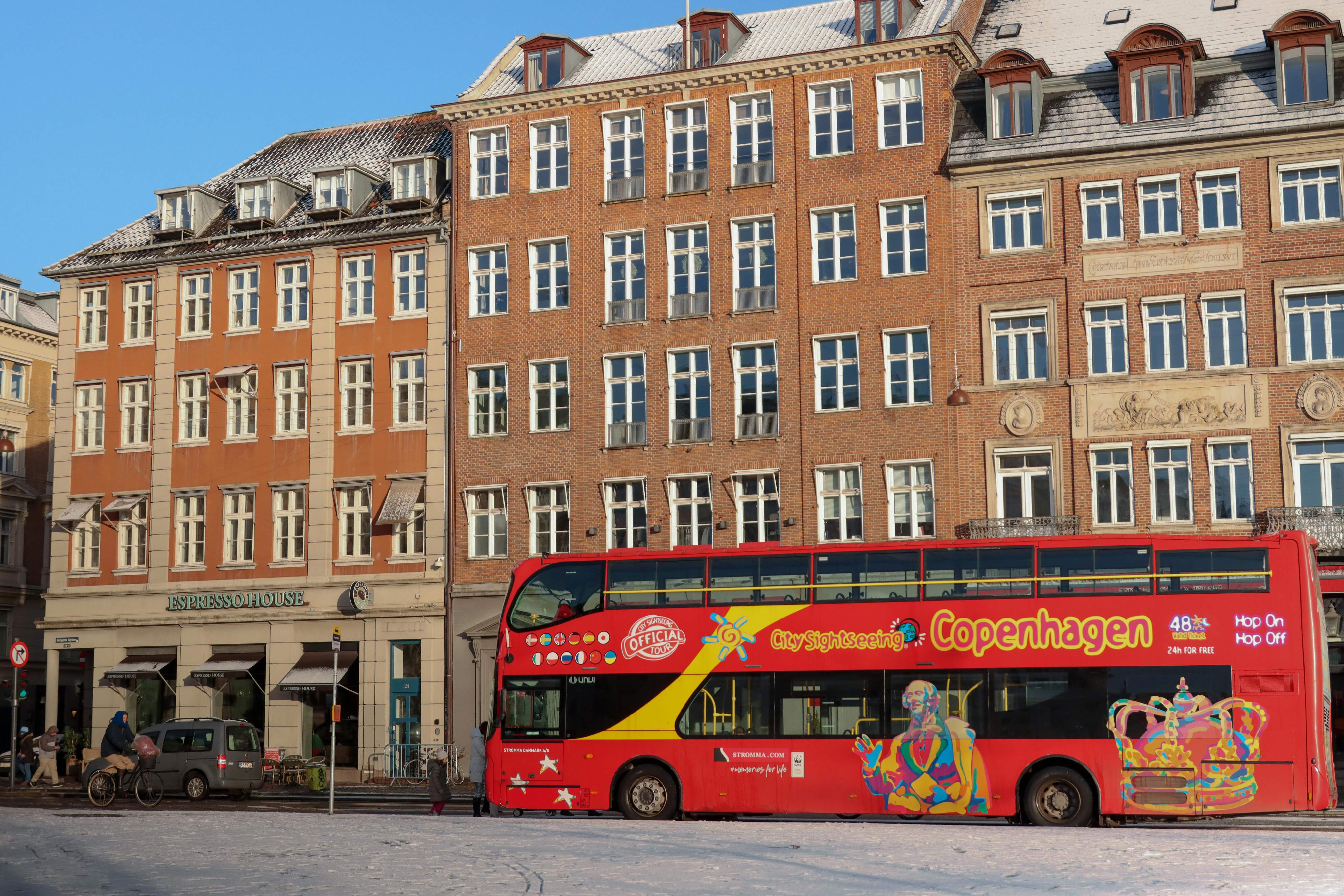 A red double-decker bus parked outside a private airport transfer service in Copenhagen.