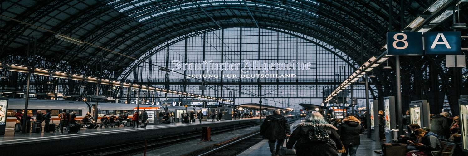 People stand in a Frankfurt train station, featuring a large glass window that allows natural light to fill the space.