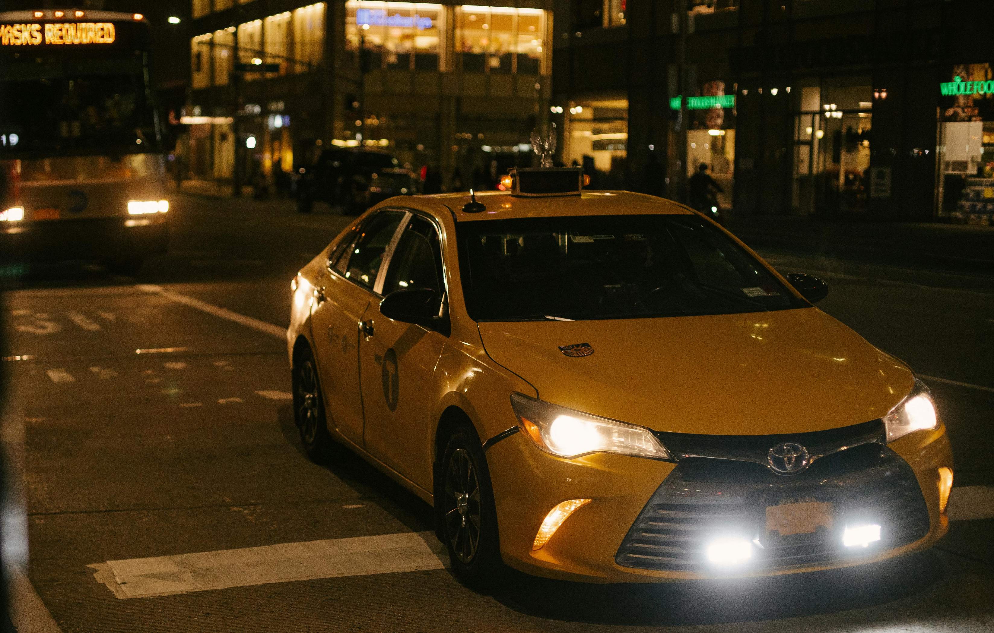 A yellow taxi from Frankfurt drives down a street illuminated by city lights at night.