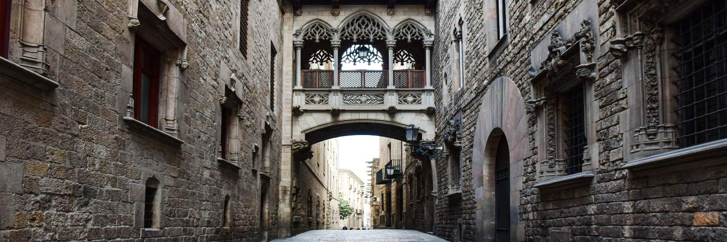 A narrow alleyway in the Gothic Quarter of Barcelona, featuring stone walls and a tall archway above.