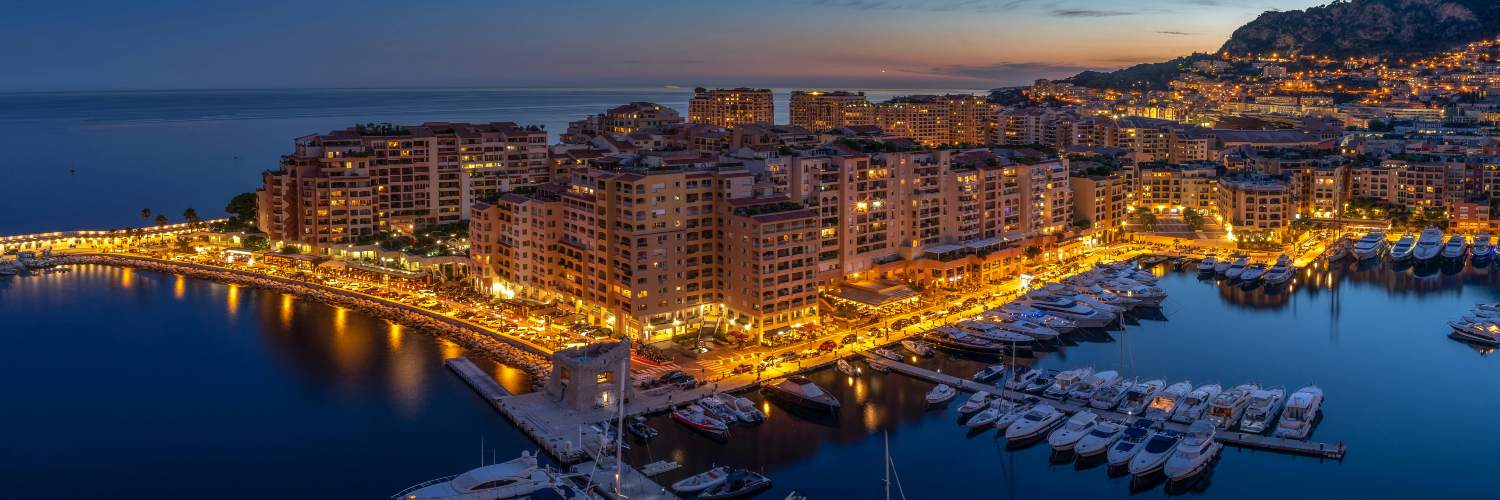 Monaco city skyline illuminated at dusk, showcasing buildings and lights against a twilight sky.