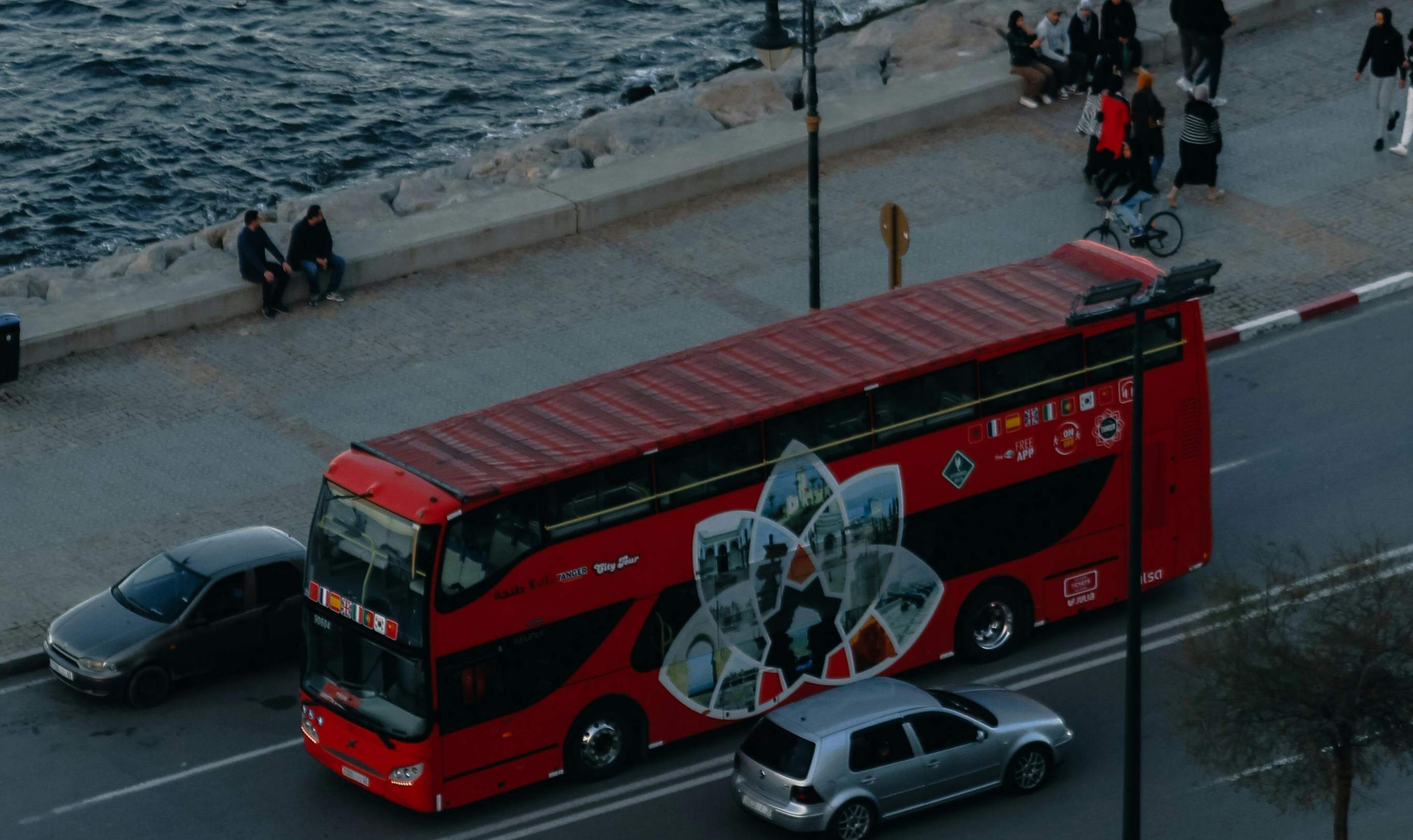 A red double-decker bus drives along the road in Monaco, showcasing the city's vibrant transportation scene.
