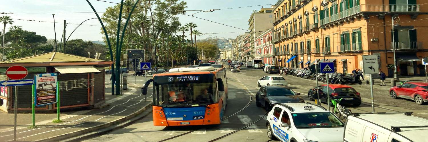 A busy street in Naples featuring a bus, cars, and trams, showcasing urban transportation.
