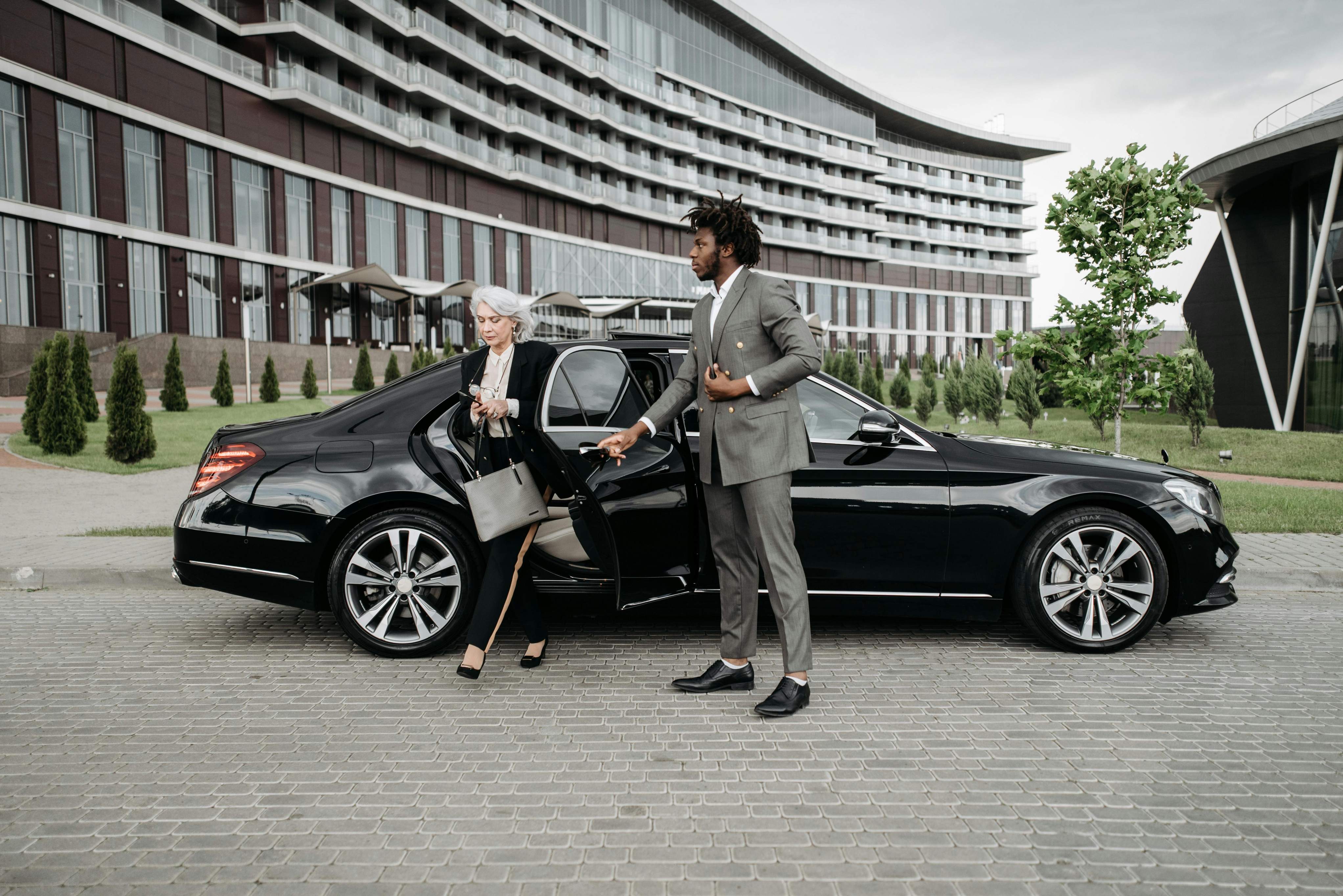 Businessman and woman entering a black car, ready for a chauffeur service after booking an airport transfer.