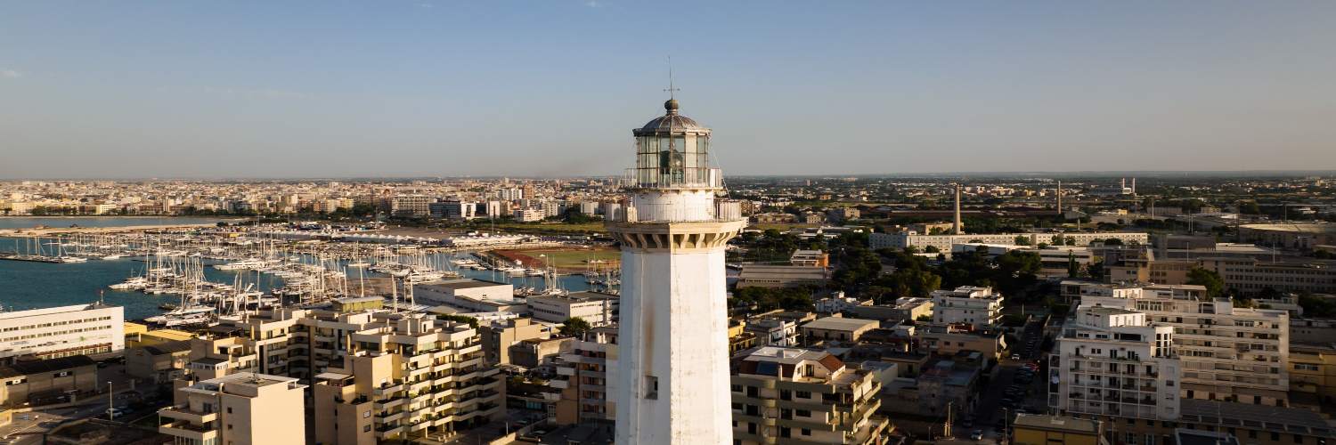 A lighthouse stands prominently in the center of a bustling city in Bali, surrounded by urban buildings and greenery.