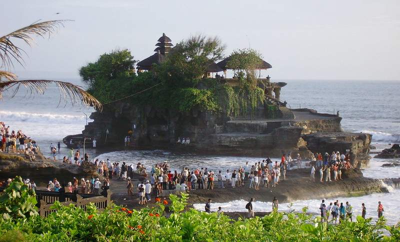 Tanah Lot Temple in Bali, a stunning sea temple perched on a rocky outcrop against a vibrant sunset backdrop.