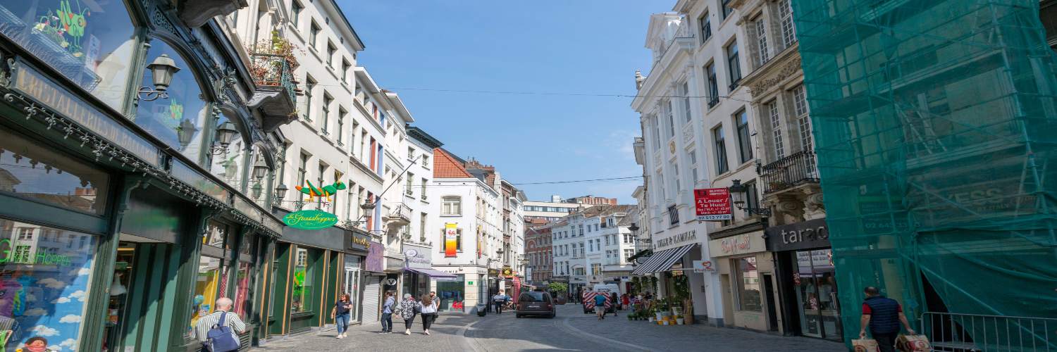 Charming Brussels street scene featuring a clear blue sky and soft white clouds above.