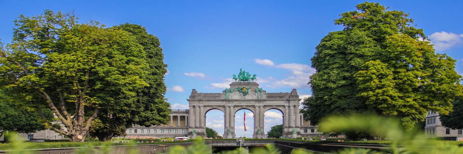 The Cinquantenaire Arch in Brussels, a grand monument symbolizing victory, framed by lush greenery and blue skies.