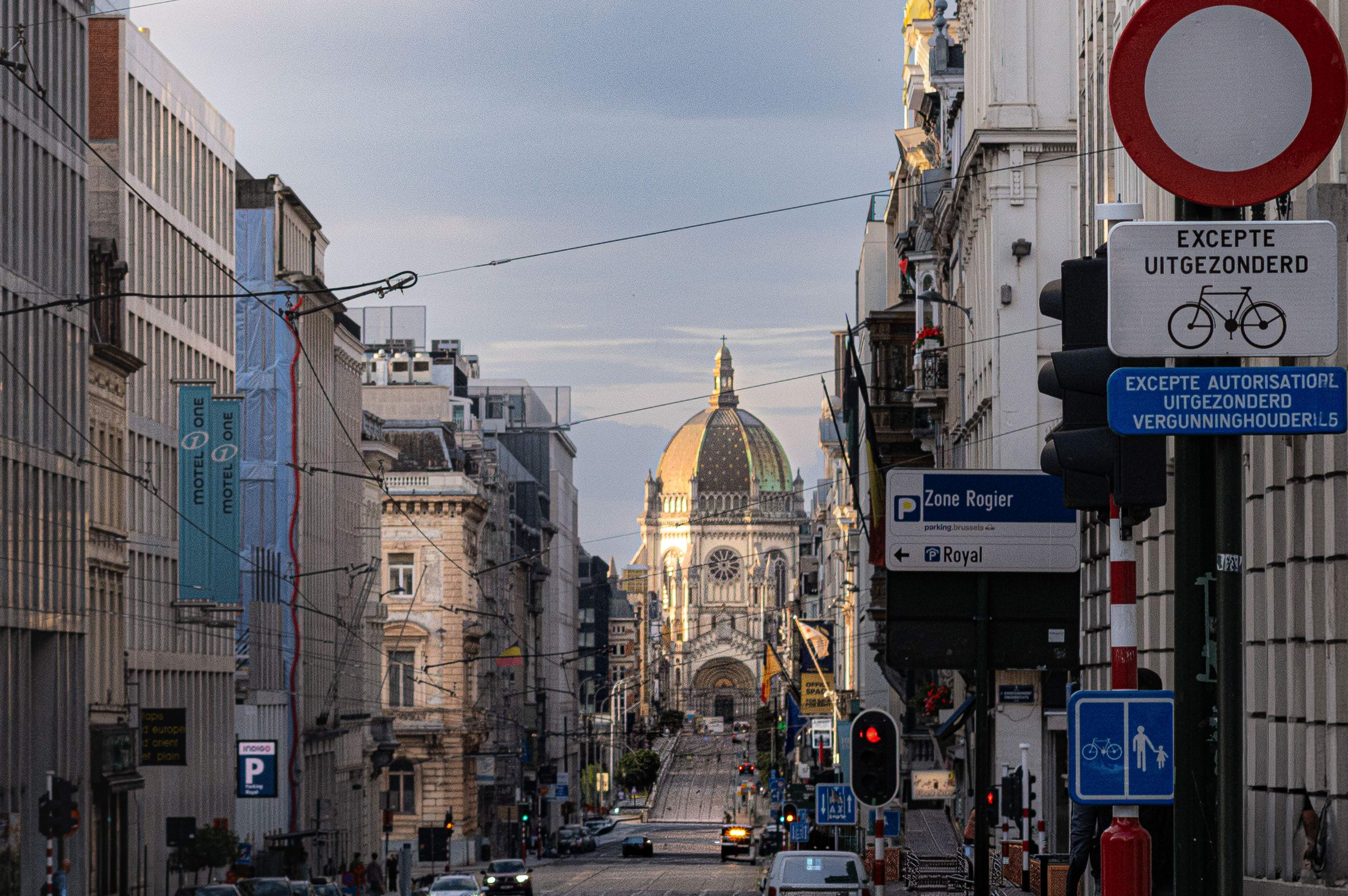 A street scene in Brussels featuring a prominent domed church in the background against a clear sky.