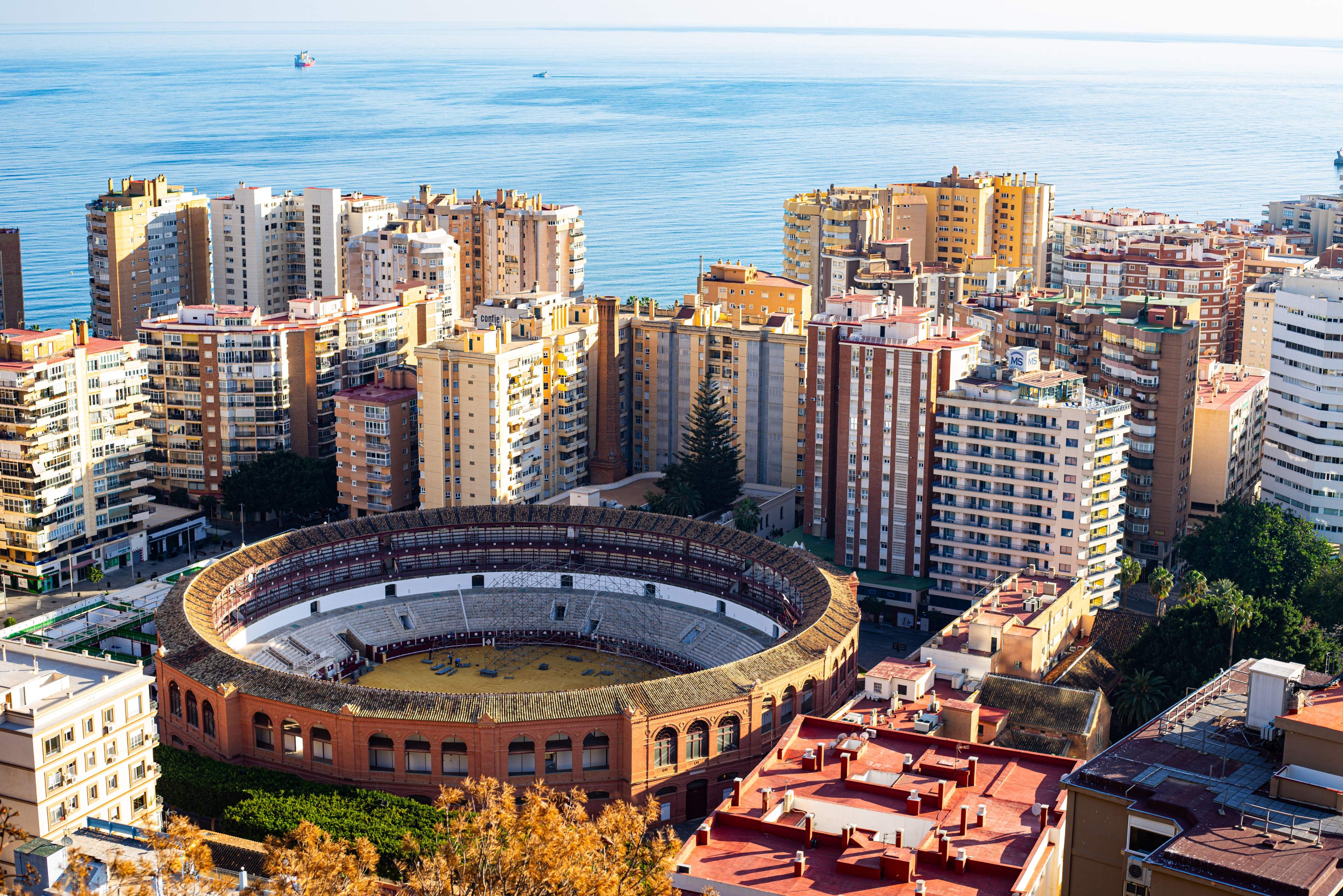The bullring in Málaga framed by urban architecture, overlooking the ocean and highlighting the city's coastal charm.
