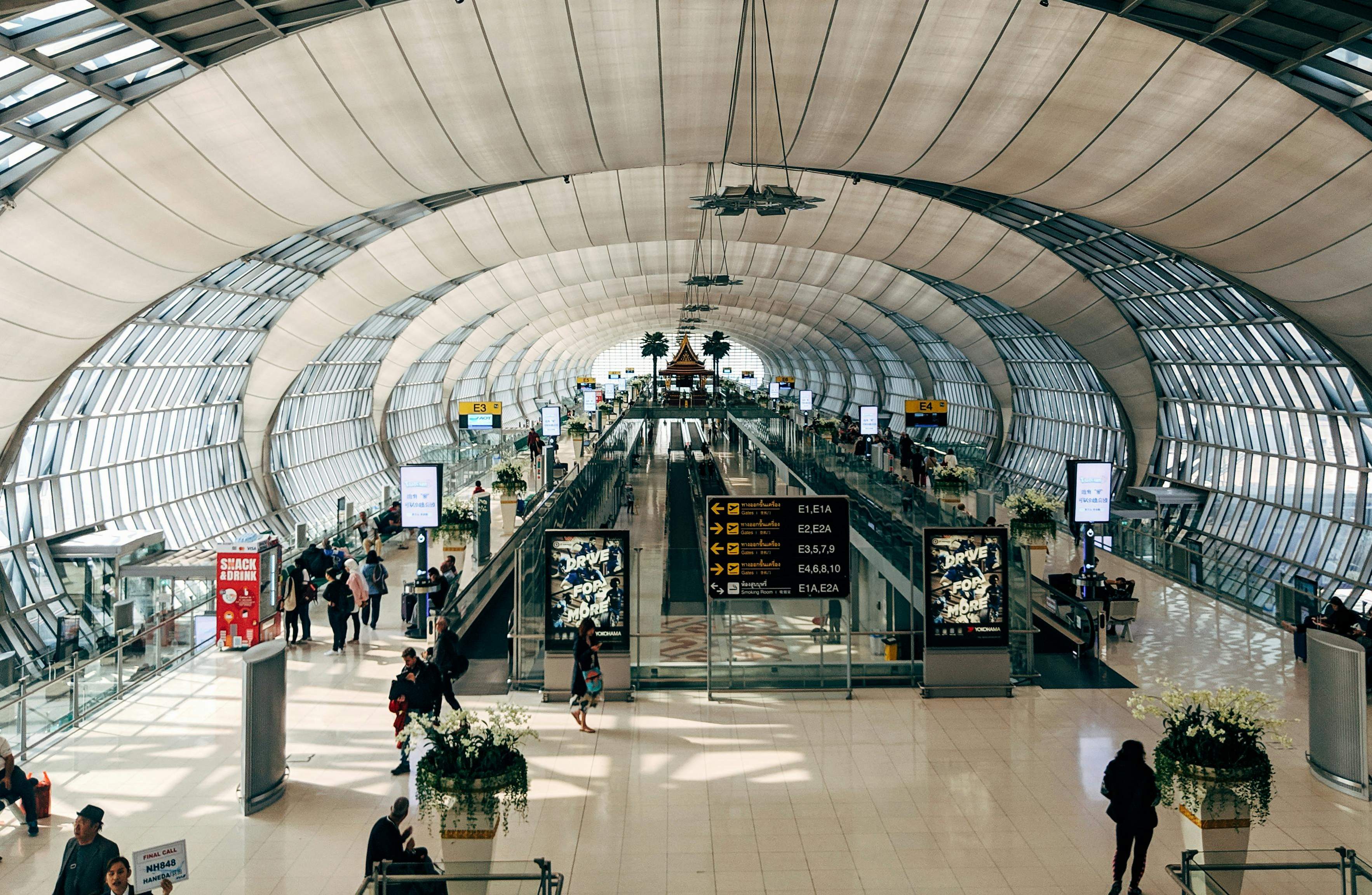 A busy airport terminal in Bangkok, with travelers moving beneath a vast ceiling, showcasing modern travel infrastructure.